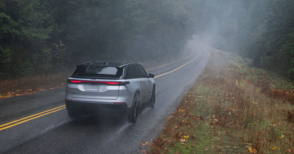 A Jeep Wagoneer driving away through rain on a foggy road.